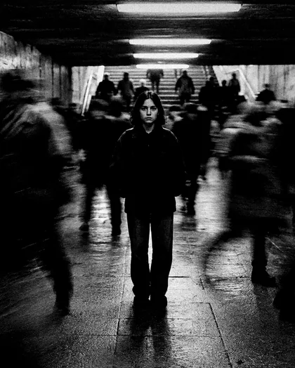 Una folla mossa in un sottopassaggio, al centro una ragazza ferma e nitida.