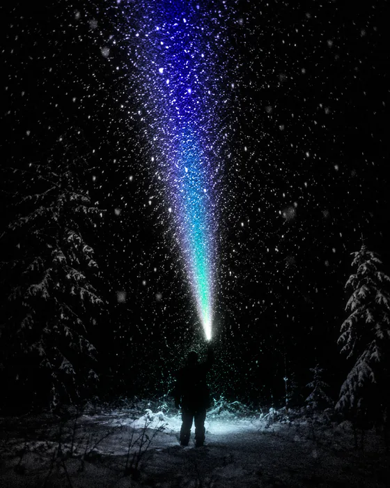 Di notte nel bosco una persona punta la torcia verso l'alto, e la neve che cade si accende di blu e di verde.