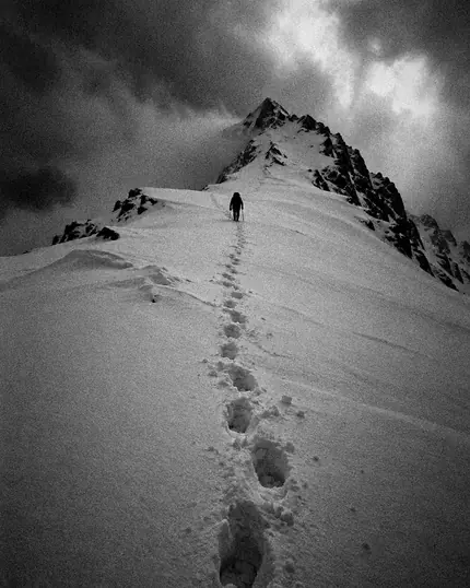 Una fila di impronte sale nella neve verso la cima, in alto una persona minuscola.
